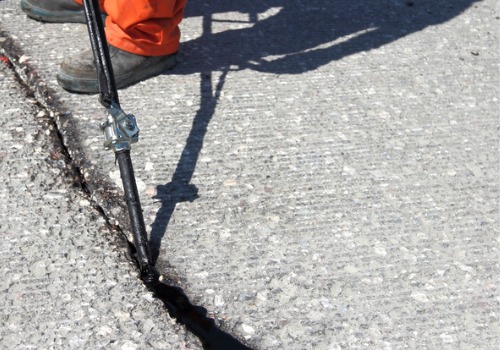 A man filling cracks in asphalt, using Top-Rated Crack Sealers manufactured by Etnyre