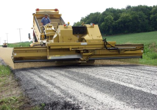 A large chip spreader covering a road with aggregate asphalt chips