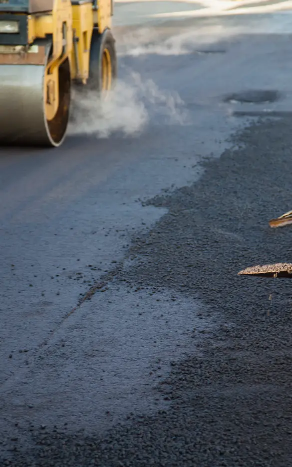 Two manual workers help level the asphalt surface before using Etnyre’s road maintenance equipment